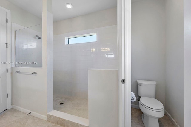 bathroom with tiled shower, toilet, and tile patterned flooring