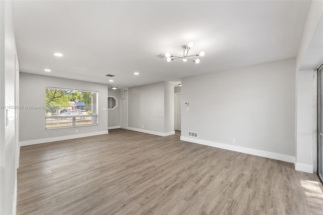 unfurnished living room featuring an inviting chandelier and light wood-type flooring