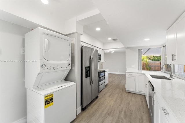 kitchen featuring white cabinets, sink, stacked washer and dryer, appliances with stainless steel finishes, and light hardwood / wood-style floors