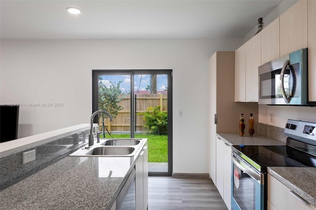 kitchen with dark stone counters, sink, light brown cabinetry, appliances with stainless steel finishes, and light hardwood / wood-style floors