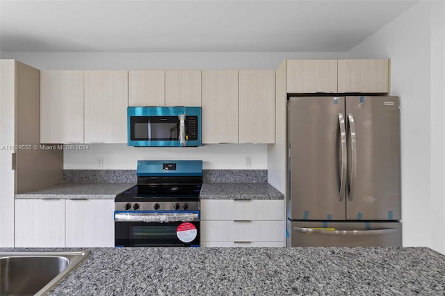 kitchen featuring light brown cabinets, dark stone countertops, and stainless steel appliances