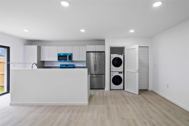 kitchen with white cabinets, sink, stacked washer and dryer, appliances with stainless steel finishes, and light hardwood / wood-style floors