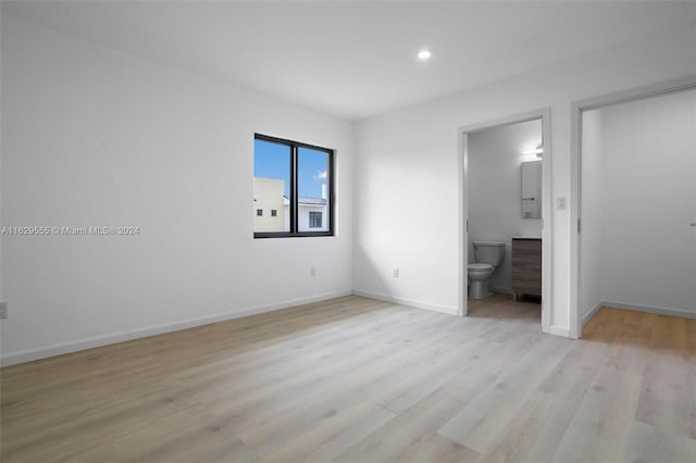 unfurnished bedroom with ensuite bathroom and light hardwood / wood-style floors