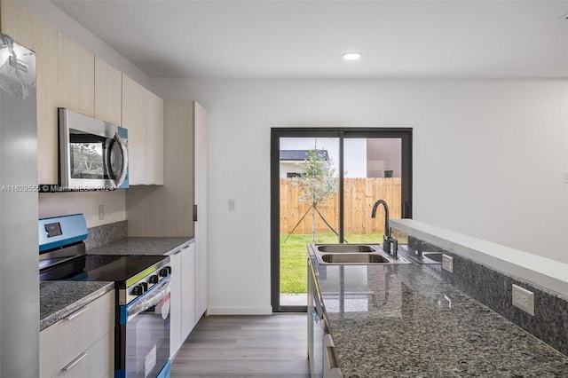 kitchen featuring dark stone countertops, a healthy amount of sunlight, stainless steel appliances, and light wood-type flooring