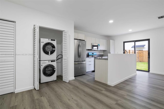 kitchen featuring white cabinets, stacked washer / drying machine, stainless steel appliances, and hardwood / wood-style floors