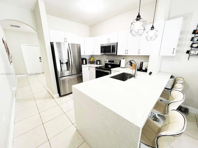 kitchen featuring hanging light fixtures, kitchen peninsula, white cabinets, and appliances with stainless steel finishes