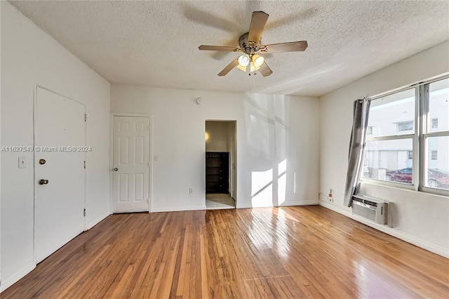 unfurnished living room with an AC wall unit, a textured ceiling, ceiling fan, and hardwood / wood-style floors