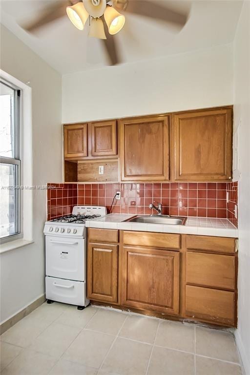 kitchen featuring tasteful backsplash, ceiling fan, tile counters, plenty of natural light, and white gas range