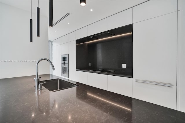 kitchen featuring white cabinets, dark stone counters, and sink