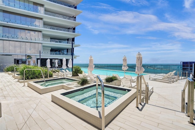 view of pool with a hot tub and a water view