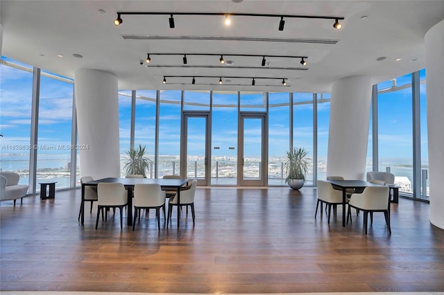 dining area with track lighting, dark hardwood / wood-style flooring, a water view, and expansive windows