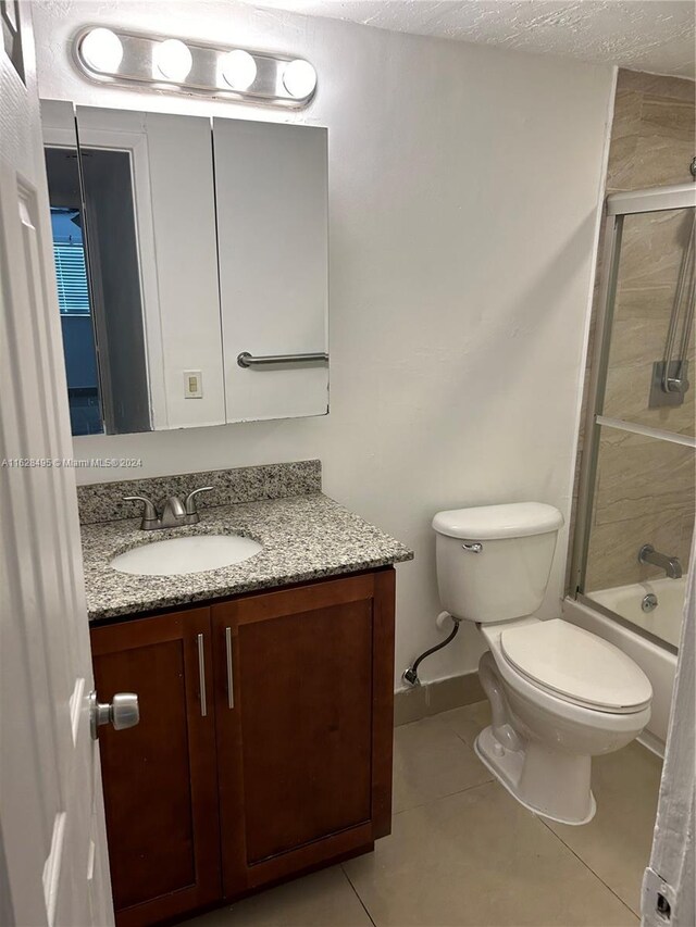 full bathroom featuring a textured ceiling, enclosed tub / shower combo, tile patterned floors, vanity, and toilet