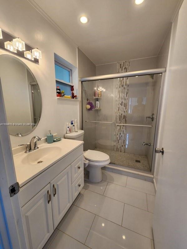 bathroom featuring vanity, an enclosed shower, tile patterned flooring, and toilet