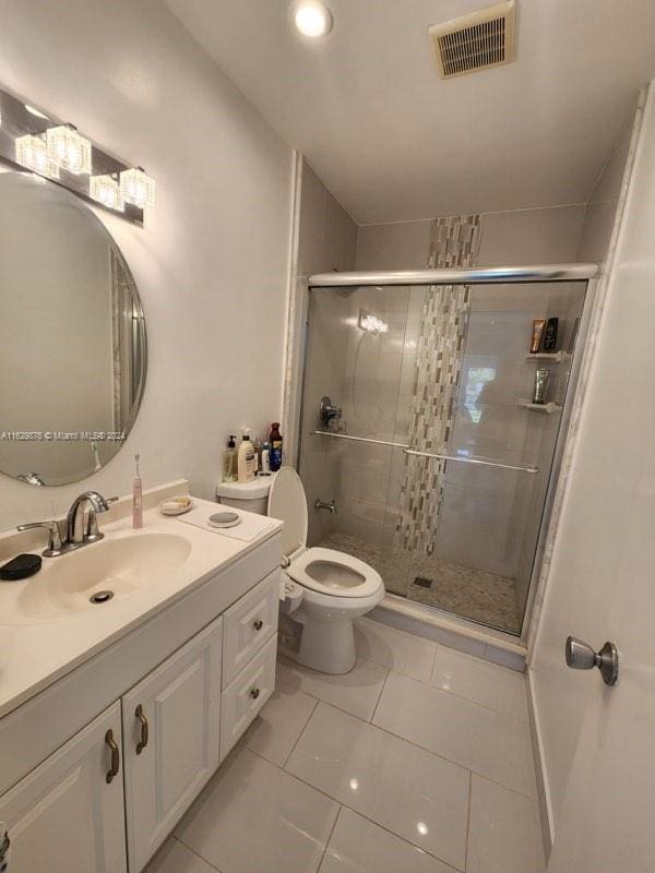 bathroom featuring tile patterned flooring, a shower with shower door, toilet, and vanity