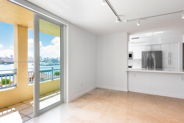 unfurnished living room featuring track lighting, a water view, and light tile patterned floors