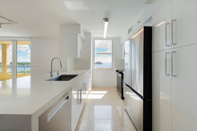 kitchen featuring stove, a sink, modern cabinets, stainless steel fridge, and dishwashing machine