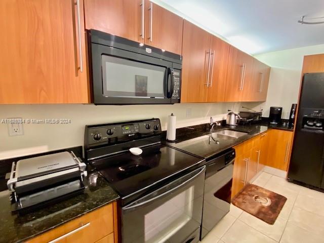 kitchen with dark stone counters, sink, light tile patterned flooring, and black appliances