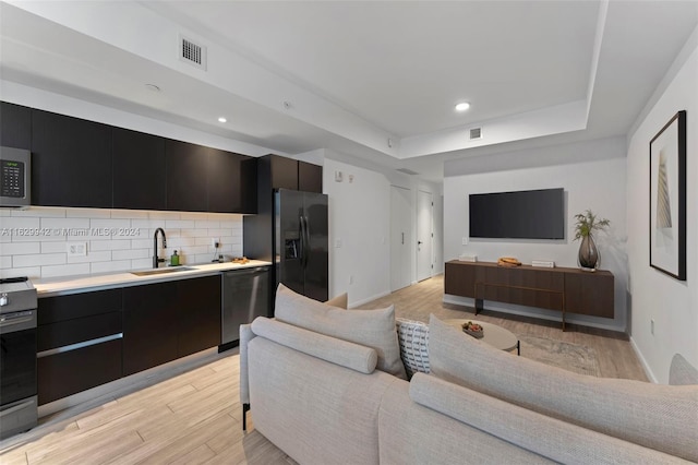 living room featuring sink, a tray ceiling, and light hardwood / wood-style floors