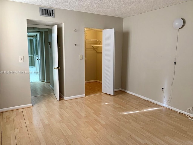 unfurnished bedroom featuring a closet, a spacious closet, a textured ceiling, and light wood-type flooring