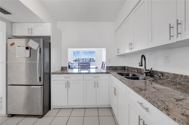 kitchen with white cabinetry, stainless steel refrigerator, light tile patterned floors, stone counters, and sink