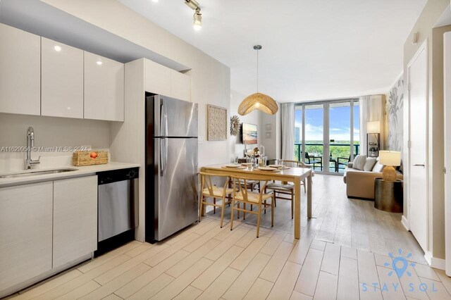 kitchen with light wood-type flooring, dishwasher, fridge, a wall of windows, and sink