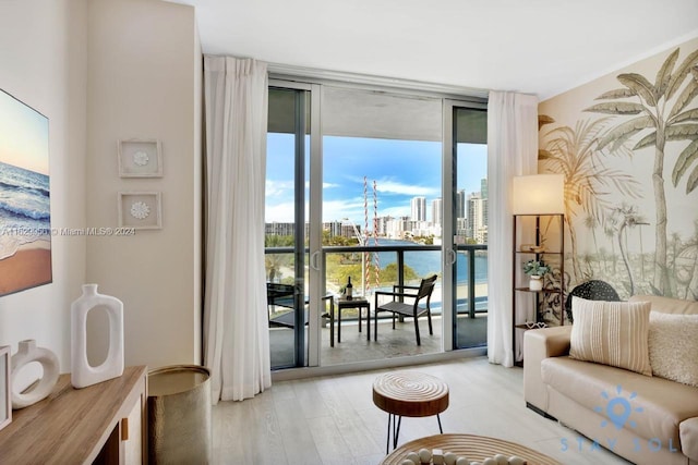 living room featuring a water view, light wood-type flooring, a wall of windows, and a city view