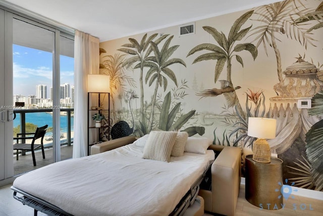 bedroom featuring a city view, a water view, visible vents, expansive windows, and access to outside