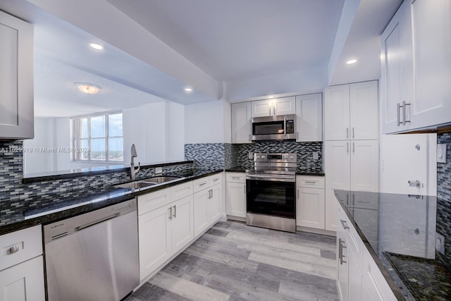 kitchen featuring appliances with stainless steel finishes, sink, decorative backsplash, light wood-type flooring, and dark stone countertops