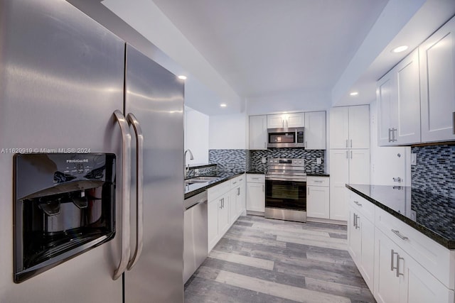 kitchen featuring appliances with stainless steel finishes, dark stone counters, sink, backsplash, and light hardwood / wood-style floors