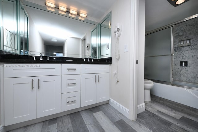 full bathroom featuring toilet, hardwood / wood-style floors, combined bath / shower with glass door, and dual bowl vanity