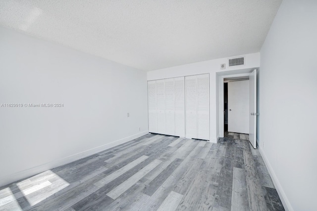 unfurnished bedroom featuring a textured ceiling, a closet, and wood-type flooring