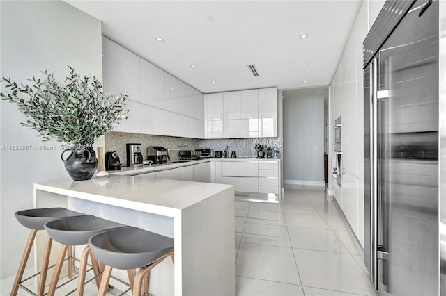 kitchen with backsplash, kitchen peninsula, white cabinetry, and a breakfast bar