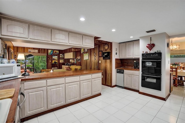 kitchen featuring black double oven, light tile patterned floors, wood counters, a notable chandelier, and wood walls