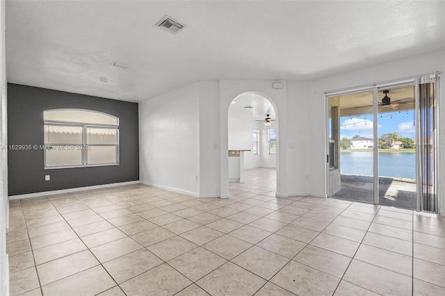 tiled empty room with a water view, a textured ceiling, and ceiling fan