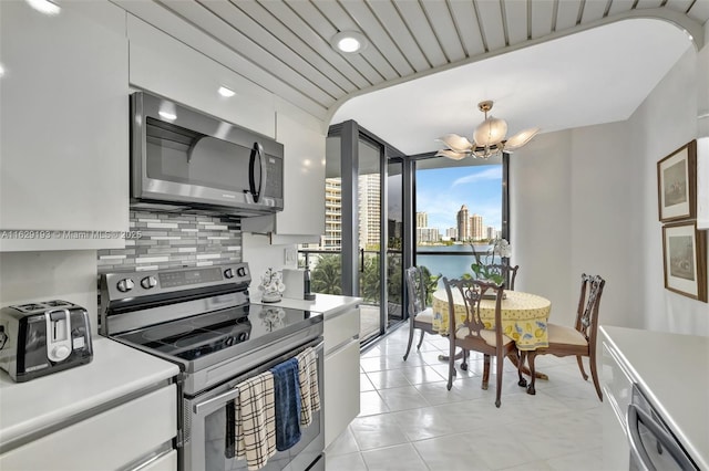 kitchen featuring decorative light fixtures, white cabinets, backsplash, a notable chandelier, and stainless steel appliances