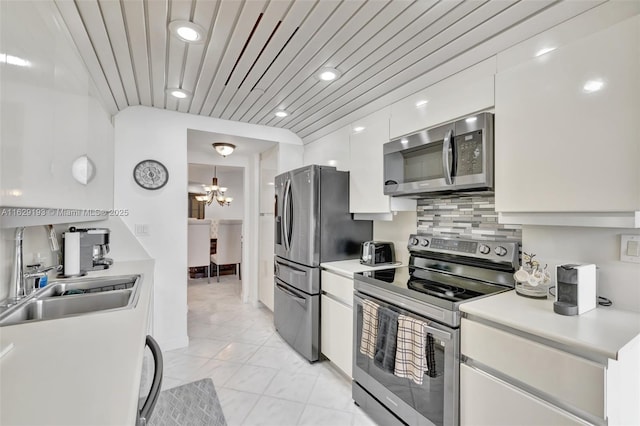 kitchen featuring sink, stainless steel appliances, white cabinets, decorative backsplash, and a chandelier