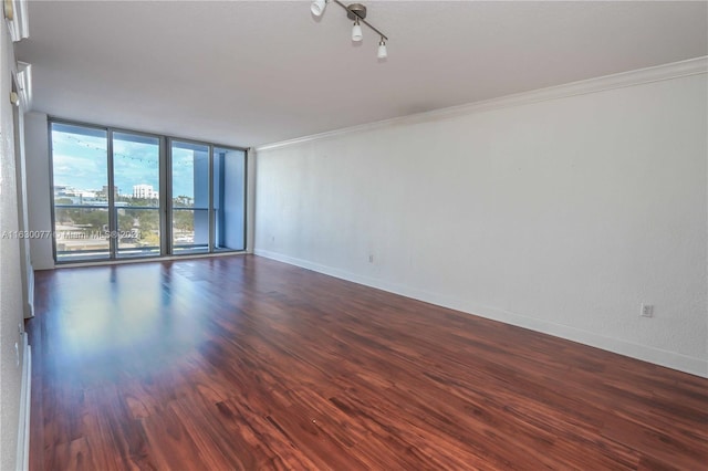 empty room with rail lighting, dark hardwood / wood-style floors, crown molding, and a wall of windows