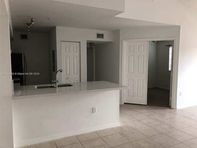 kitchen with sink, light tile patterned floors, kitchen peninsula, and black fridge