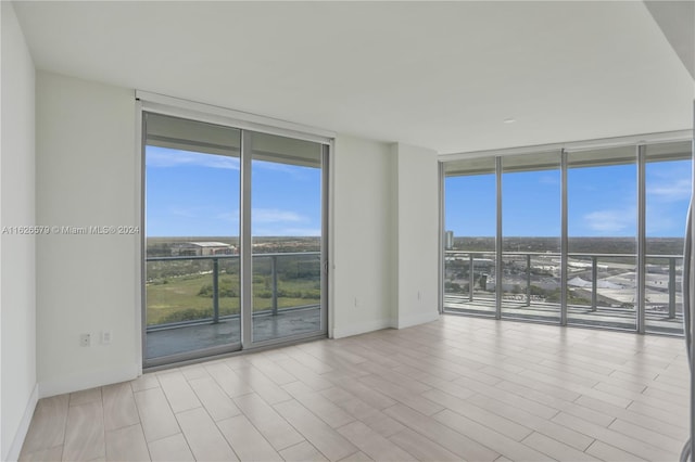 spare room with a wall of windows and light hardwood / wood-style floors