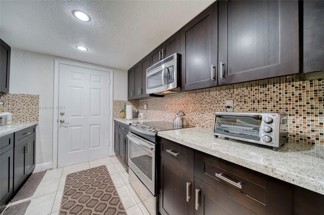 kitchen with tasteful backsplash, light stone counters, a textured ceiling, dark brown cabinets, and appliances with stainless steel finishes