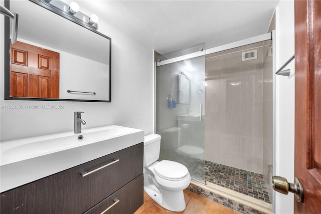 bathroom with a shower with door, vanity, toilet, and tile patterned floors