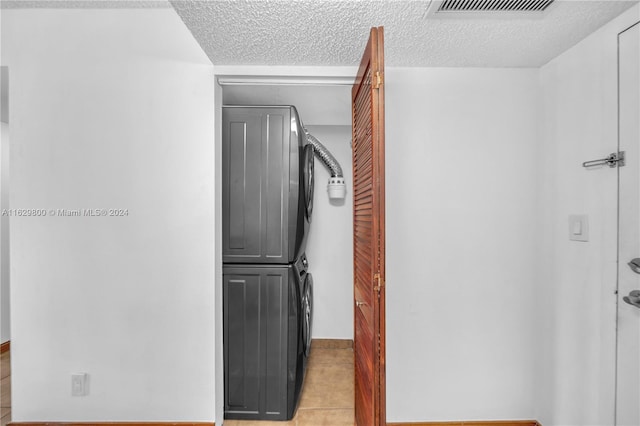 hallway featuring light tile patterned floors, stacked washer and clothes dryer, and a textured ceiling