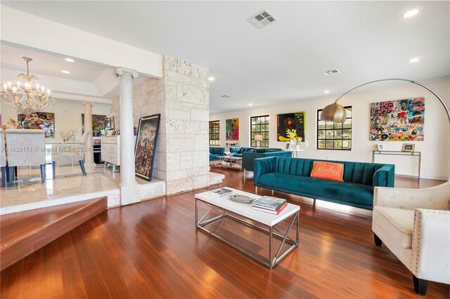 living room featuring dark wood-type flooring, ornate columns, and a notable chandelier