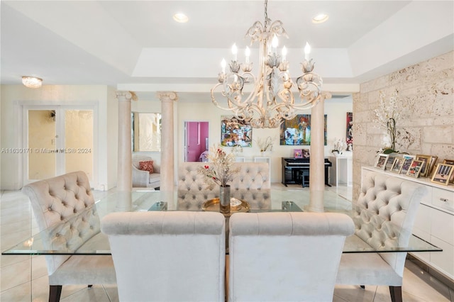 tiled dining space featuring an inviting chandelier, decorative columns, and a tray ceiling