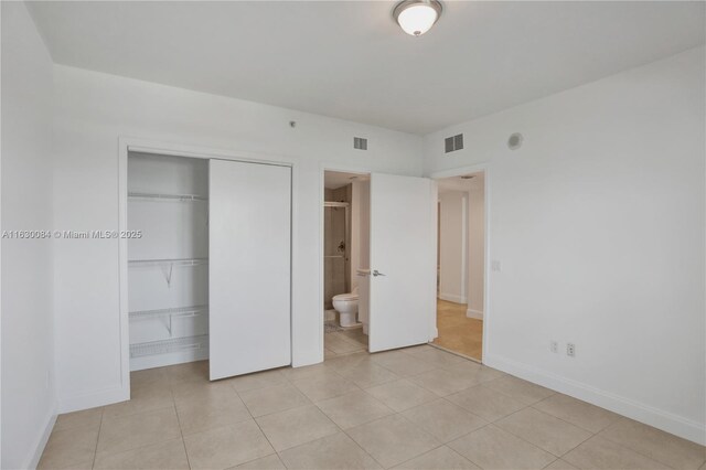 unfurnished bedroom featuring light tile patterned flooring, ensuite bathroom, and a closet