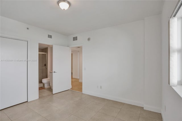 unfurnished bedroom featuring ensuite bath, light tile patterned flooring, and multiple windows