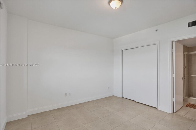 unfurnished bedroom featuring light tile patterned floors, a closet, and ensuite bathroom