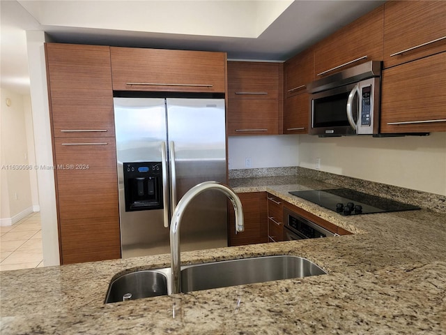 kitchen with sink, stone counters, stainless steel appliances, and light tile patterned floors