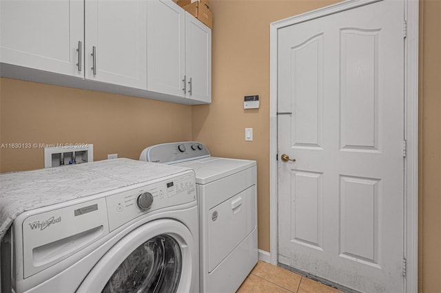 clothes washing area featuring separate washer and dryer, light tile patterned floors, and cabinets