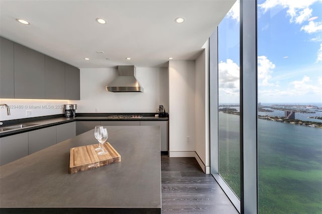 kitchen featuring gray cabinets, dark hardwood / wood-style flooring, wall chimney exhaust hood, sink, and gas stovetop